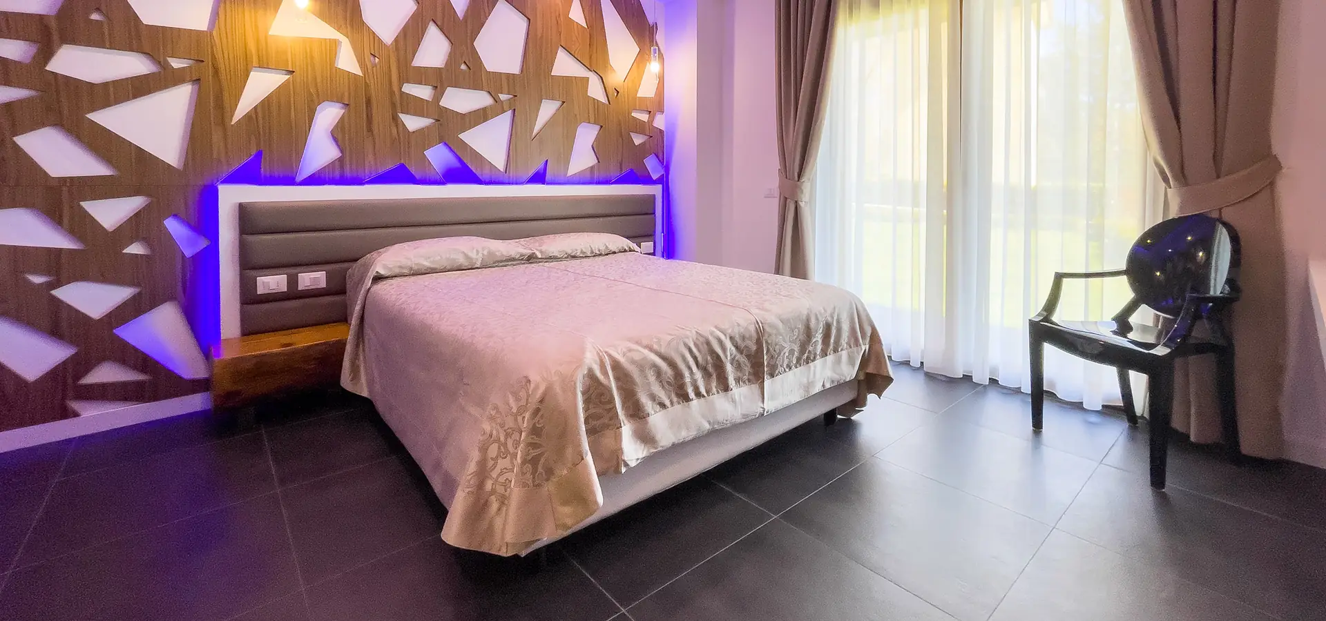 camera matrimoniale del B&B Luna per Te con parete in legno intarsiato e luci viola